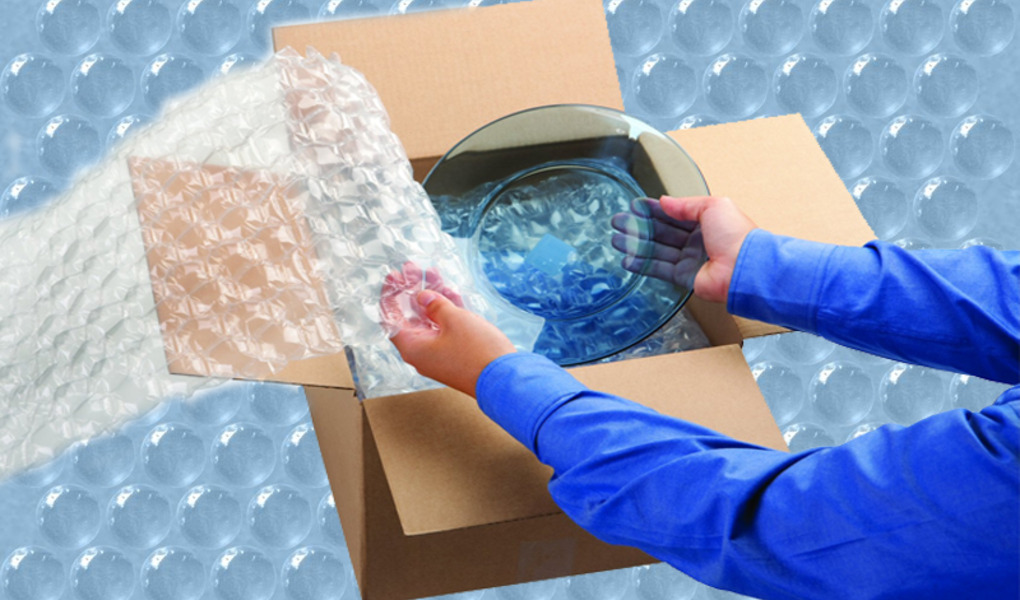 Hands wrapping a glass dish in bubble wrap inside a moving box